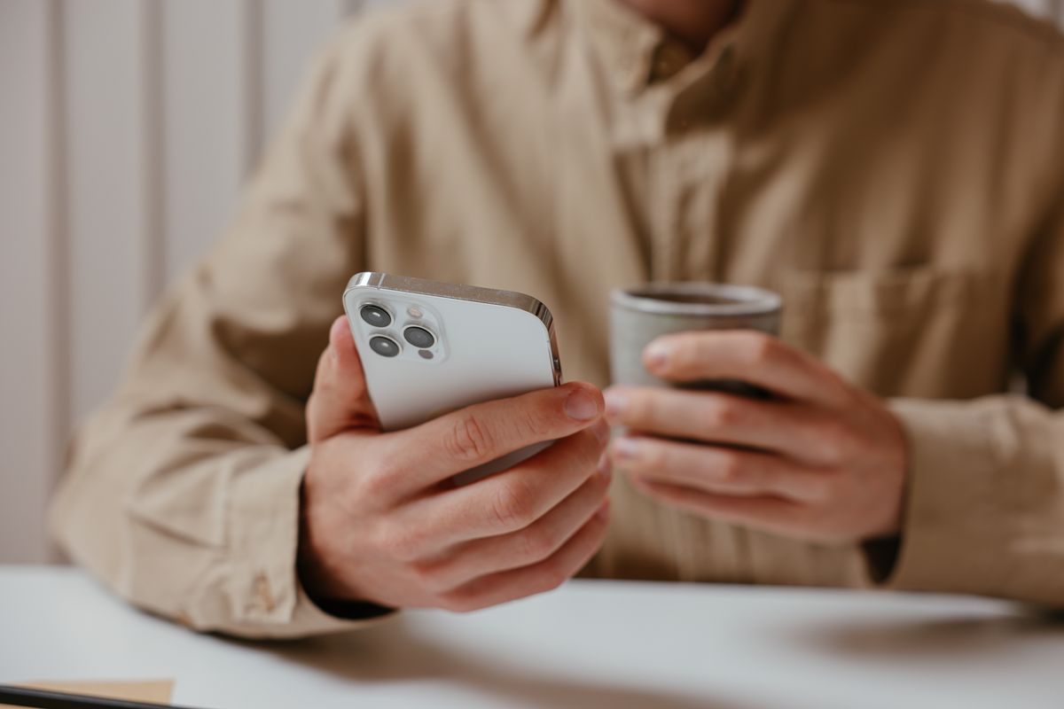 Persona con un iPhone y una taza de café en una mesa