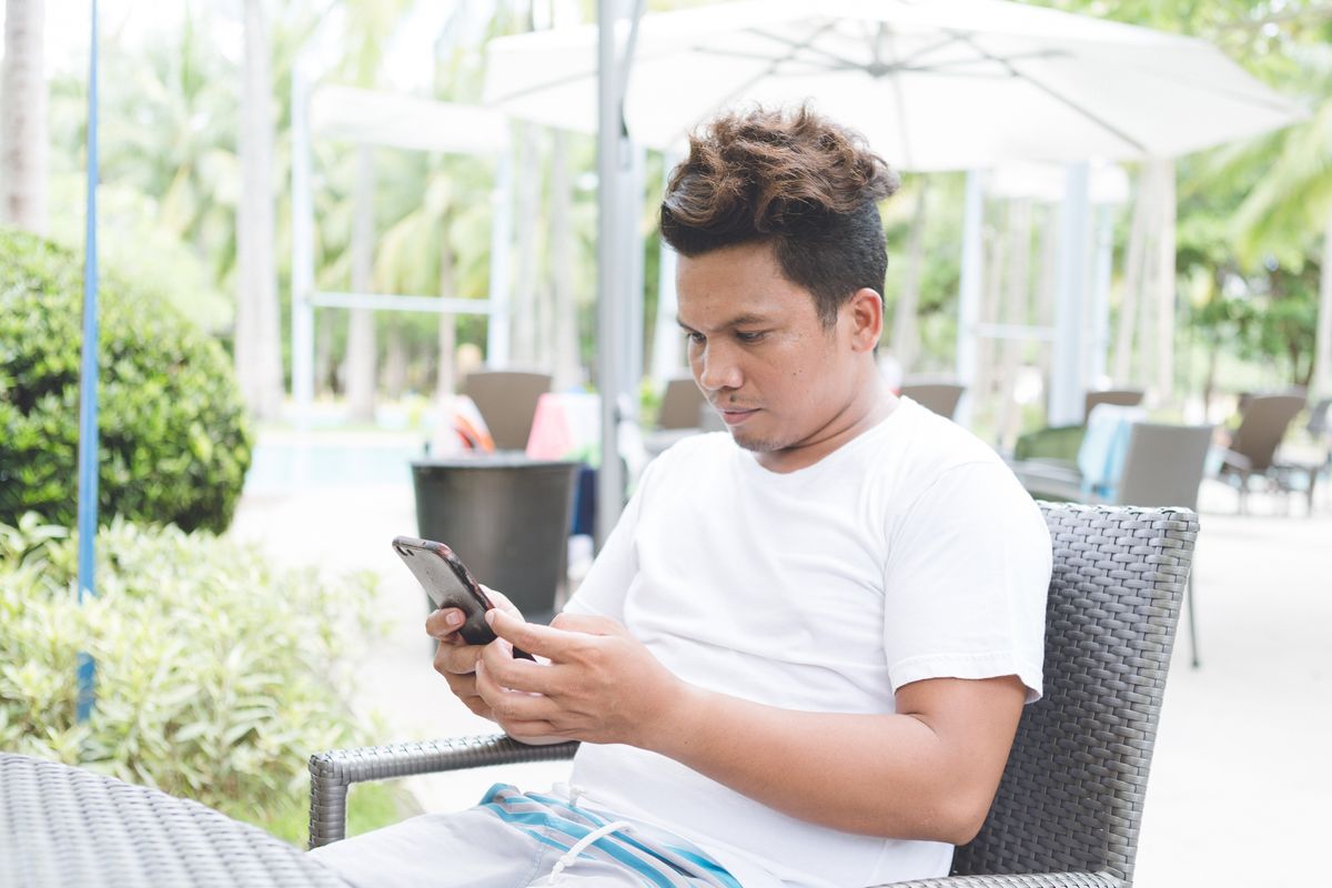 Man texting on his phone at an outdoor cafe table on vacation