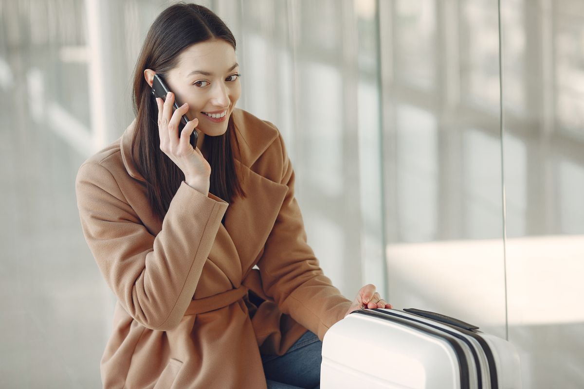 Traveller with a suitcase talking on her smartphone while waiting at an airport