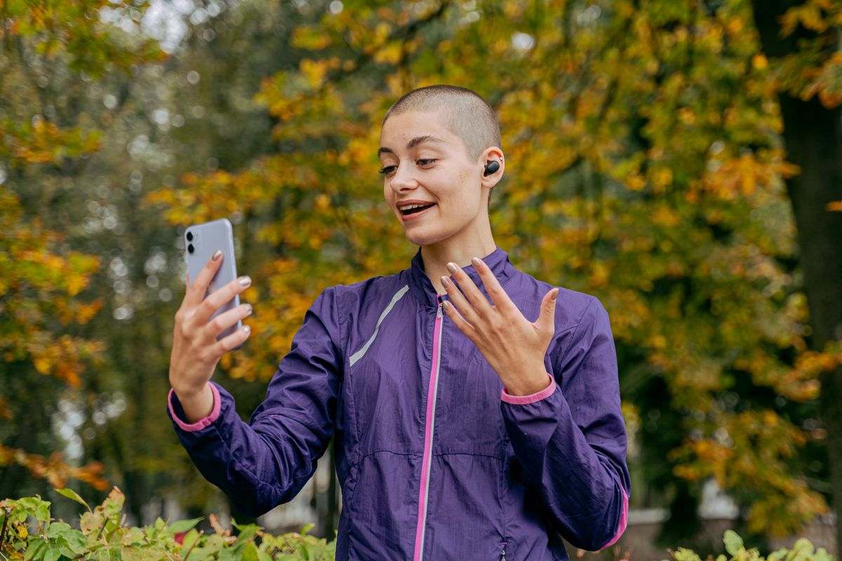 Donna con una giacca viola che fa una videochiamata con lo smartphone in un parco in autunno