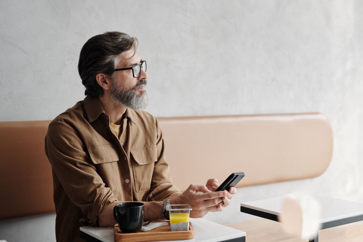 Man sitting in a cafe with a coffee, holding his smartphone
