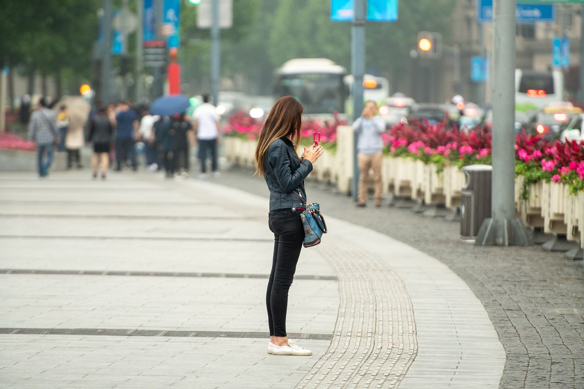 Young woman checking her phone on a busy city street while travelling