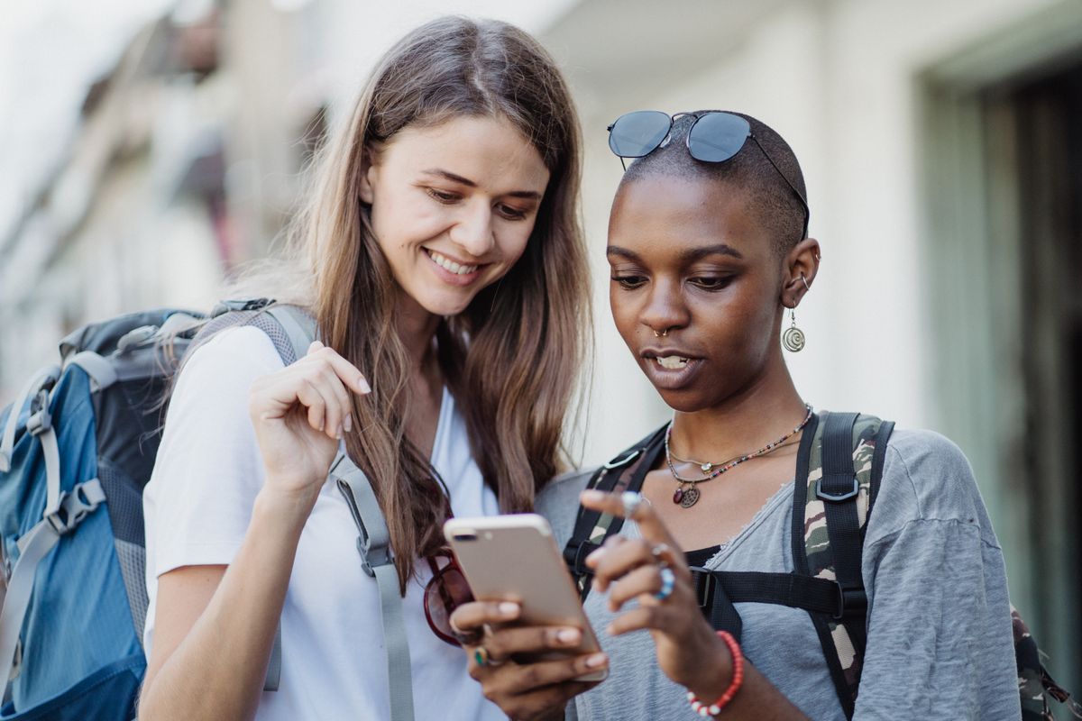 Two travellers with backpacks looking at a smartphone together in a city street
