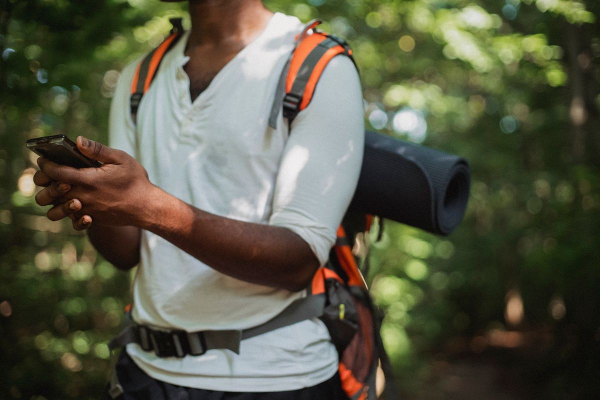 Hiker with a backpack checking his phone in a forest with weak signal