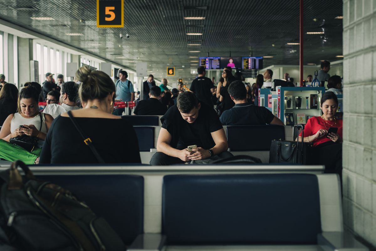 Viajeros sentados en la sala de embarque de un aeropuerto mirando sus teléfonos