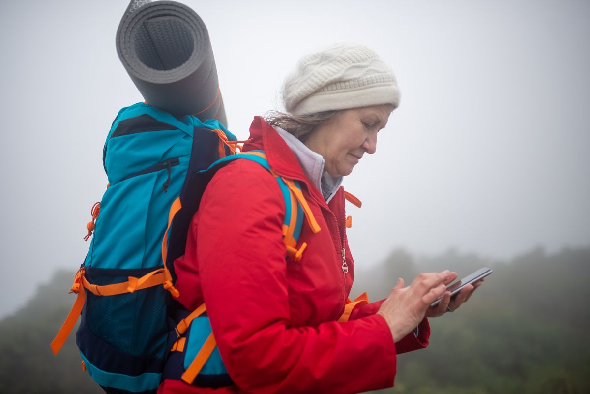 Hiker in a red jacket checking her phone on a foggy mountain trail