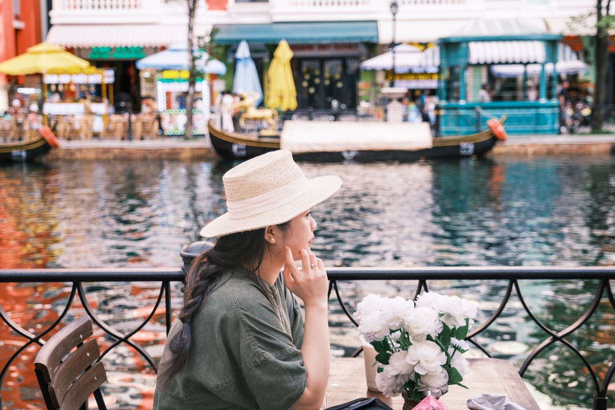 Donna con cappello di paglia che si rilassa al tavolino di un caffè sul fiume in una giornata di viaggio lento