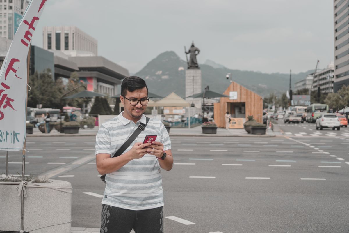 Man in a striped shirt texting on his phone in a city square