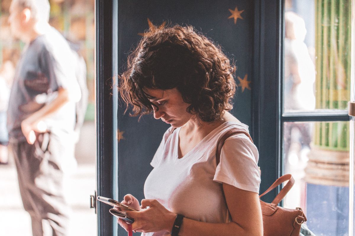 Femme qui regarde son smartphone, debout dans l'embrasure d'une porte