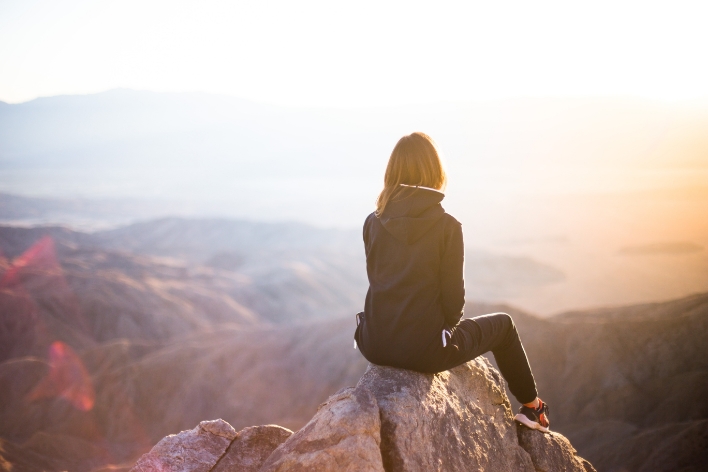 image d'une personne assise sur un rocher et regardant le coucher de soleil